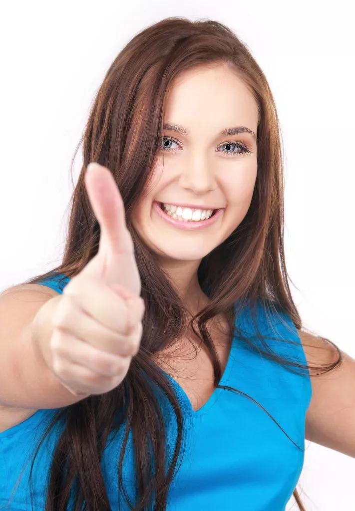 Lächelnde junge Frau in einem blauen Hemd, die vor einem weißen Hintergrund einen Daumen hoch zeigt und so die fröhliche Stimmung von SmileCover perfekt einfängt.